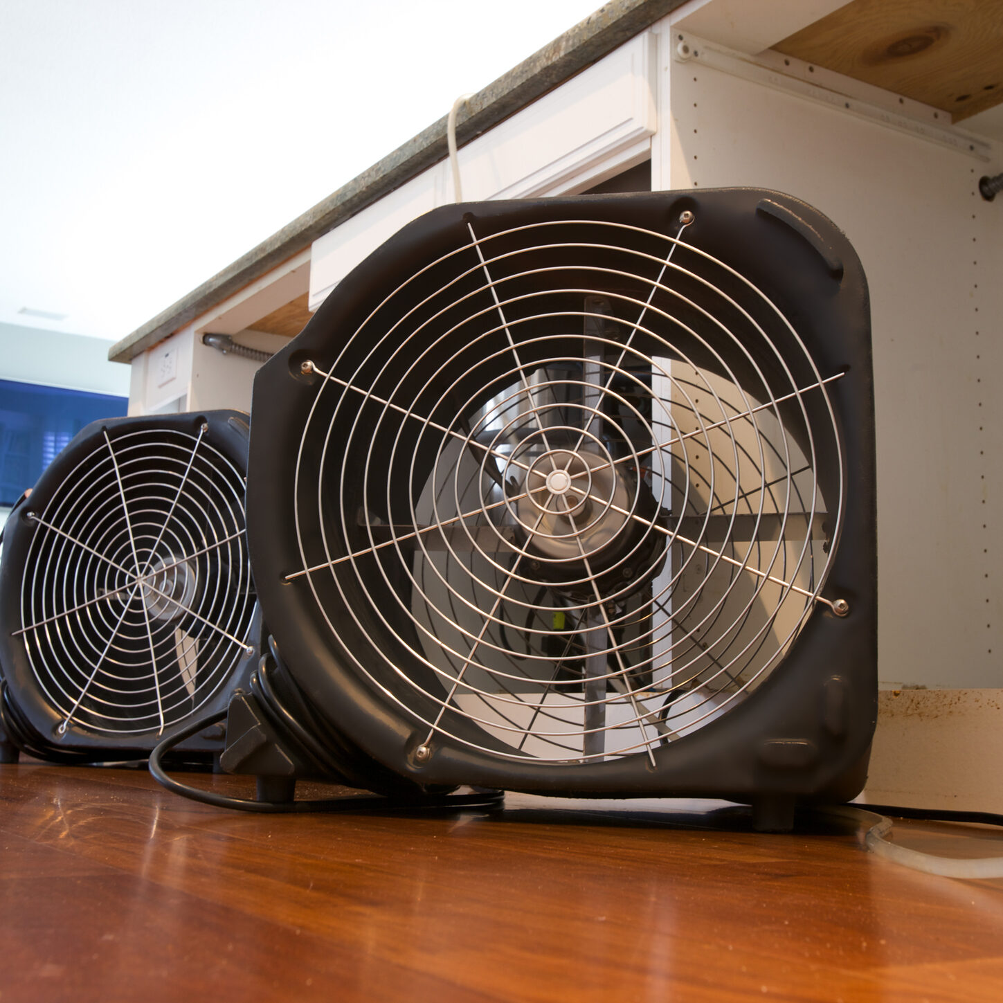Two industrial fans running to dry out water damaged residential kitchen island from leak.